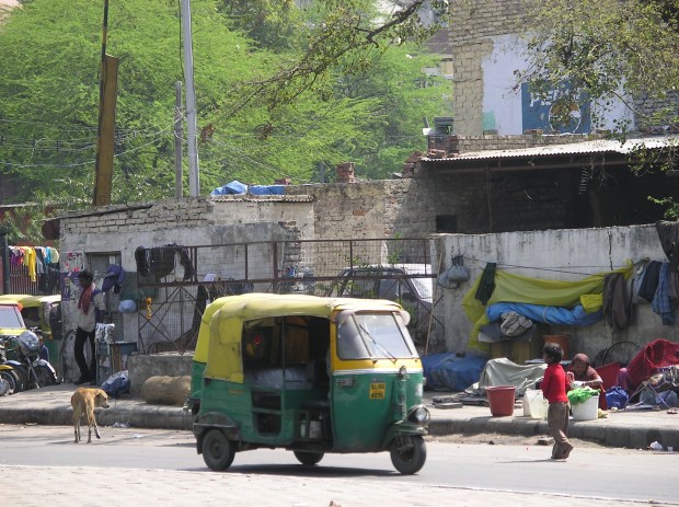 A street scene in Delhi, with an auto rickshaw passing street dwellers. Poverty is found everywhere.